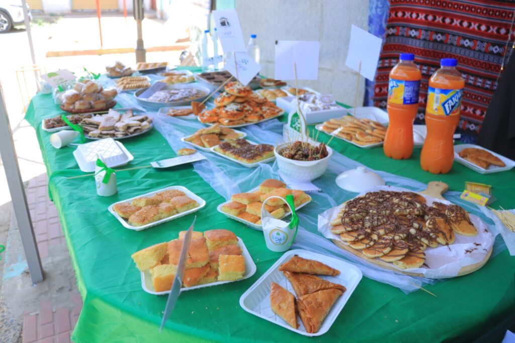 Outdoor buffet table with a variety of pastries and cookies on green tablecloth, two Fanta bottles in the background.