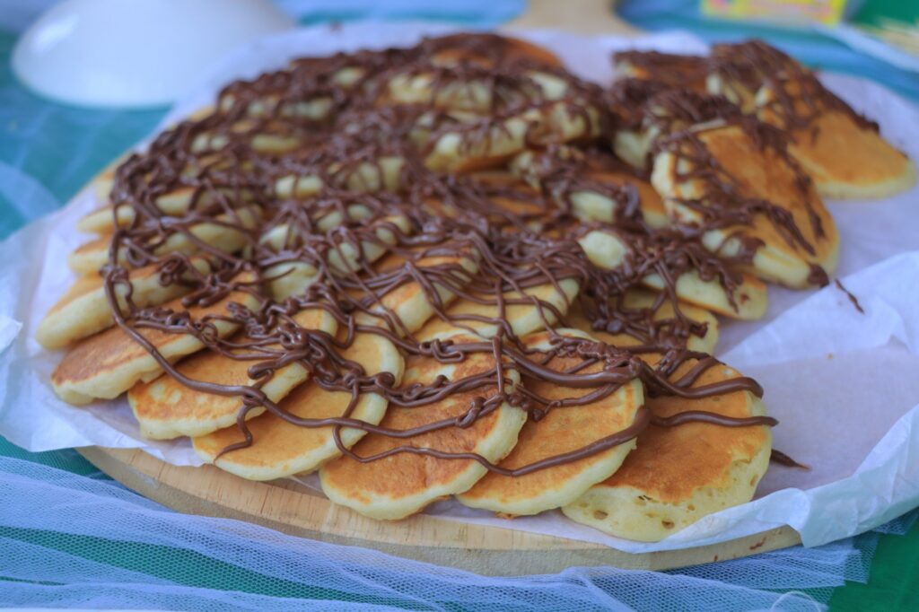 Stack of mini pancakes arranged in a circle, drizzled with chocolate and scattered apple pieces
