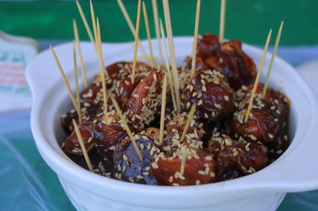 Skewered glazed dates sprinkled with sesame seeds in a white serving bowl to be eaten as a snack