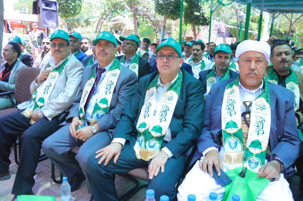 Group of men in suits wearing green scarves and caps at an outdoor ceremony or event.