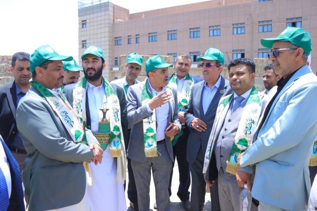 Group of men in suits wearing green hats and scarves, gathered outdoors for a ceremonial event outside a building.