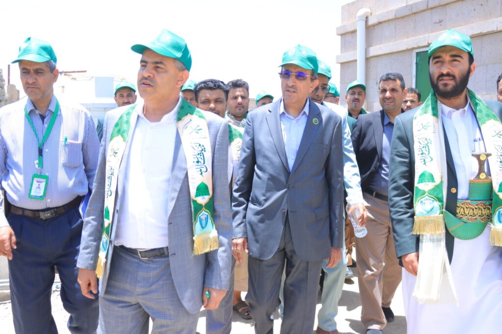 Group of men in suits wearing green caps and ceremonial sashes walking outdoors at a formal event.