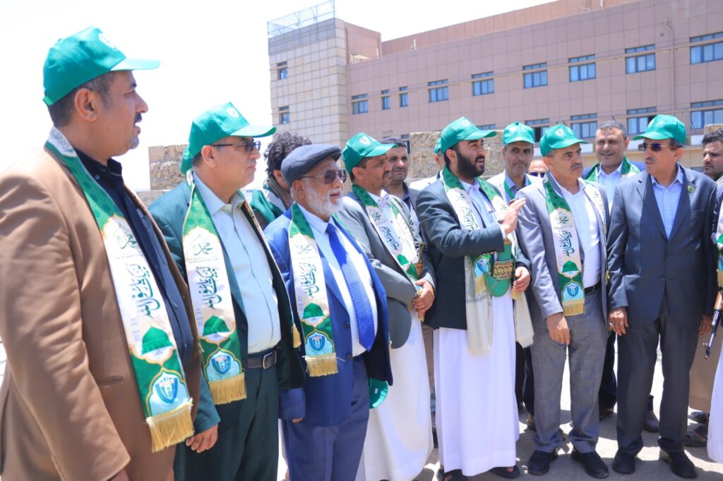 Group of men in green caps and patterned scarves standing outdoors at a formal event, near a beige building.