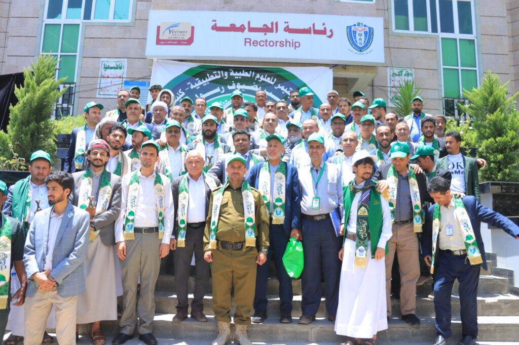 Group photo of university staff and students wearing green scarves and caps, gathered on steps in front of the Rectorate building for an event.
