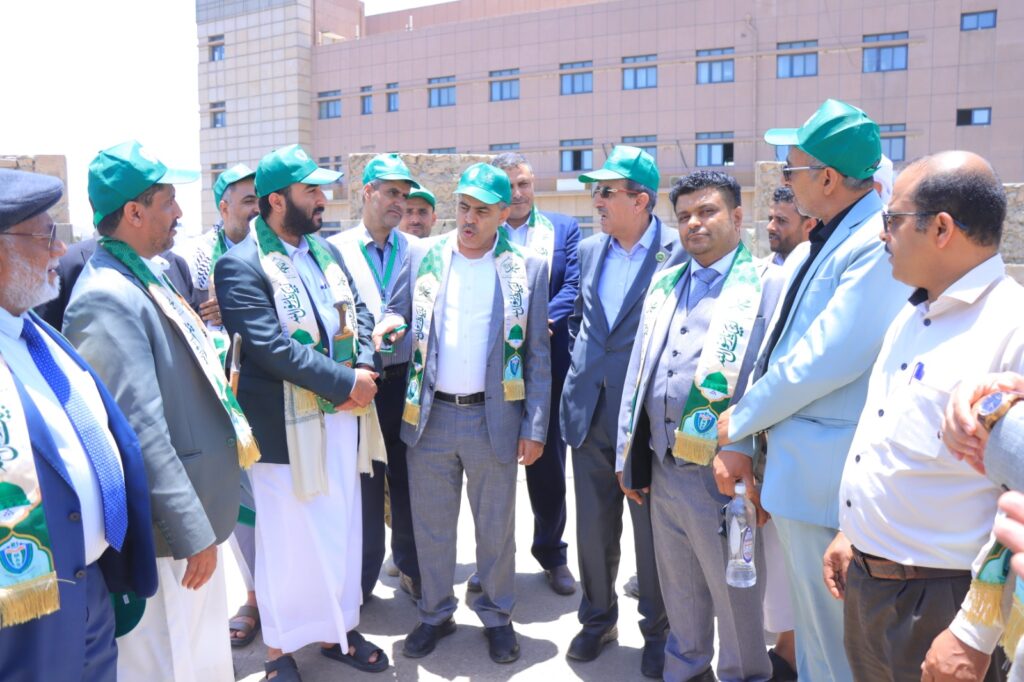 Group of men in green hats and scarves standing in a circle, talking outdoors near a building.