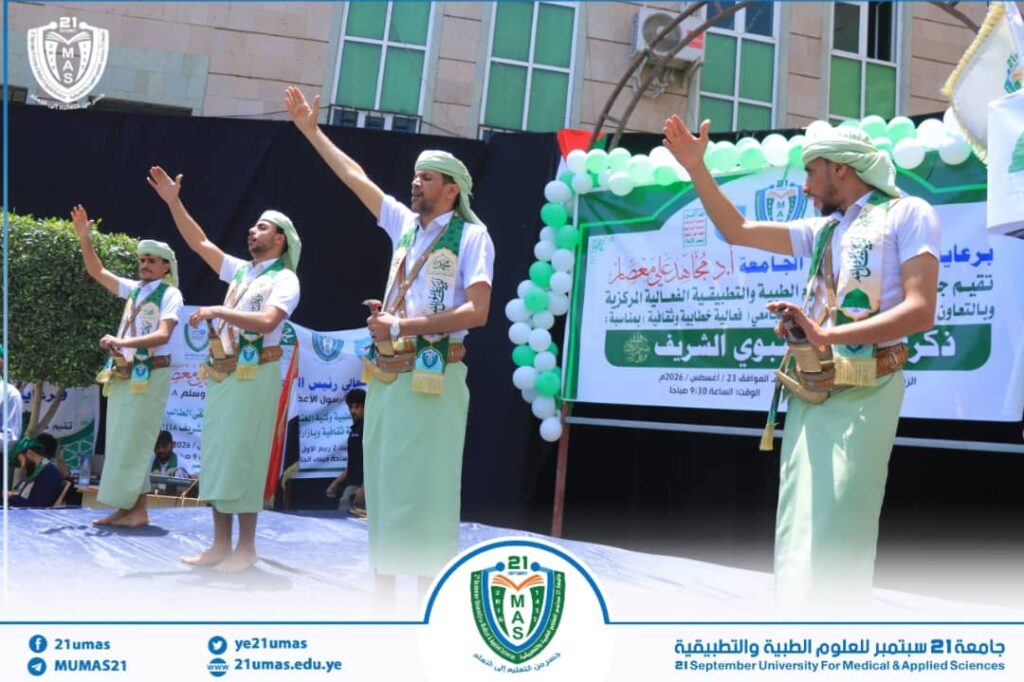 Four men in white shirts and green headbands perform a traditional sword dance on a stage at a university cultural event, with a banner and balloons in the background.