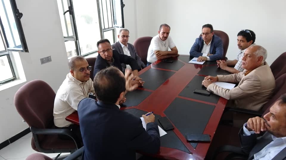 Group of professionals seated around a large conference table in a meeting room, discussing and taking notes.