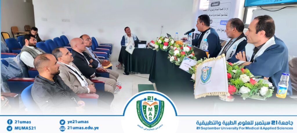 Panel of speakers seated at a long table with microphones and flower garlands, addressing an audience in a conference room. (Informative)