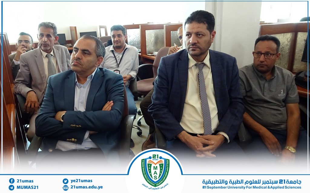 Group of men in business attire seated in a conference room, listening attentively; a university logo and Arabic text appear along the bottom border.