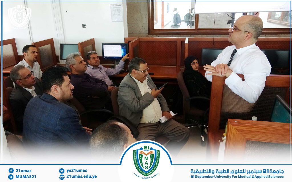Instructor in a white shirt presents to a seated group in a university computer lab.
