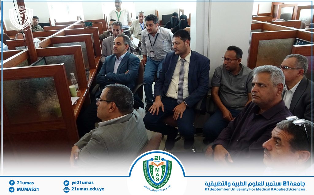Group of professionals seated in a conference room with wooden cubicles; several men in suits and a few women in niqab in the back.