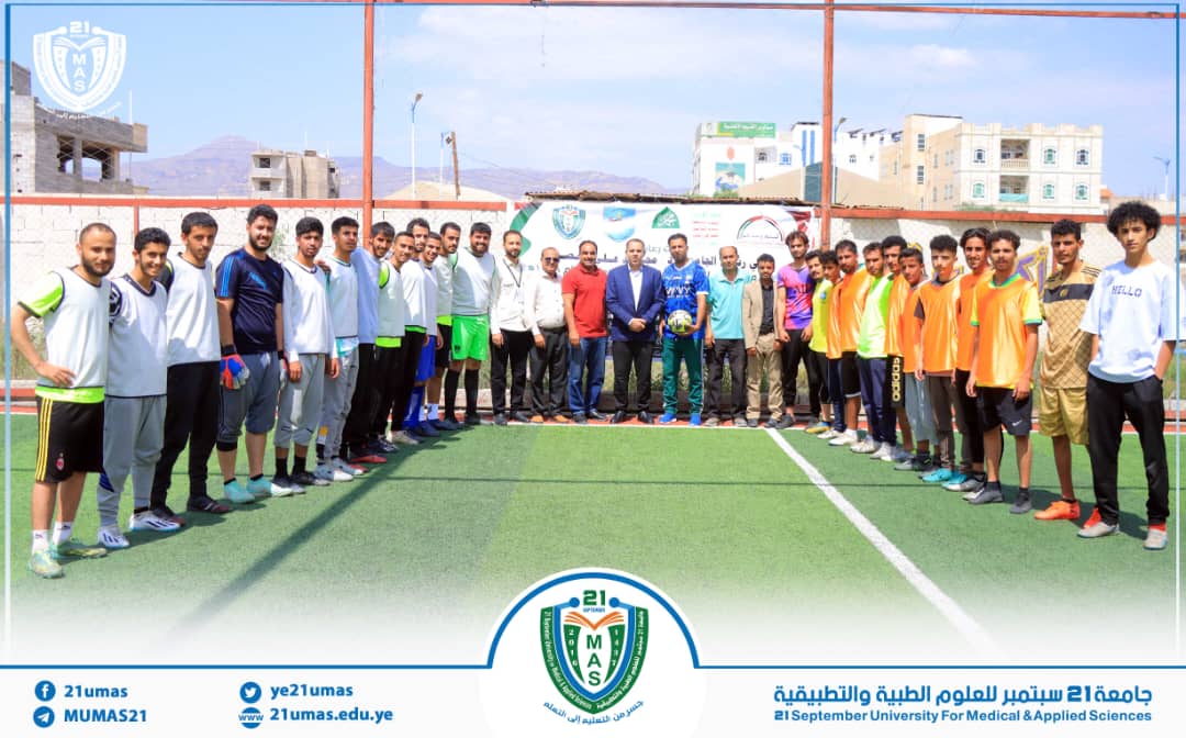 Group of students and staff on a soccer field posing for a campus event, with a banner and university emblem behind them.