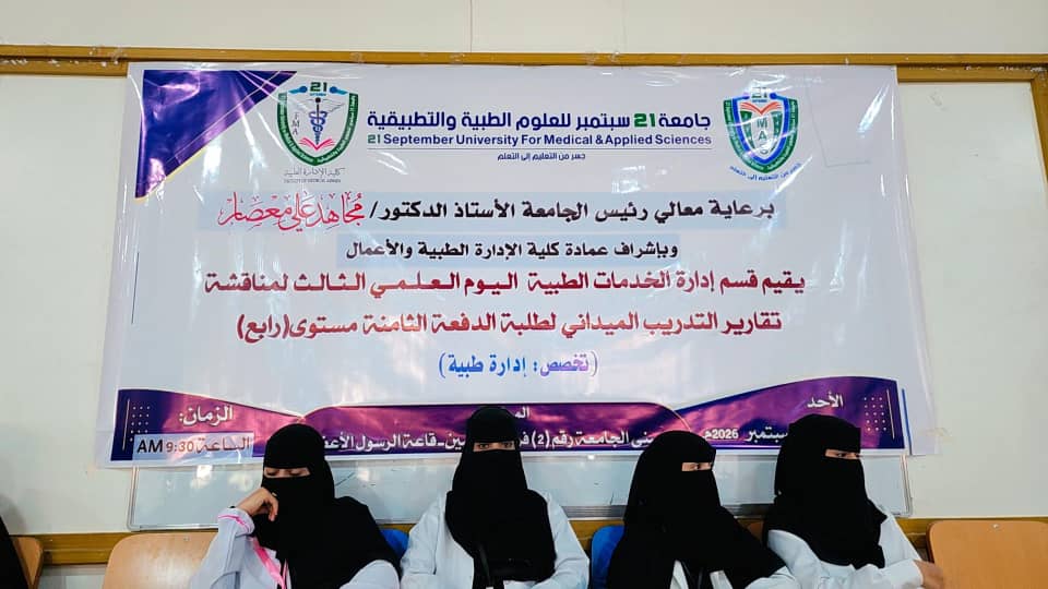 Four women wearing black niqabs sit in front of a large banner for 21 September University for Medical & Applied Sciences.