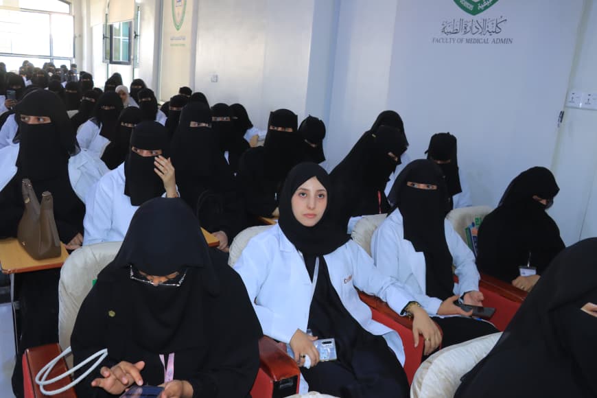 Group of female students wearing black hijabs and white coats sit in a bright classroom, attending a lecture at a medical faculty.