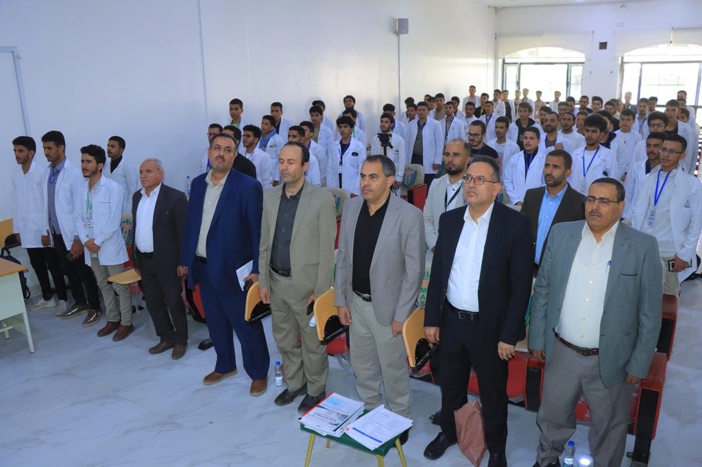 Group of men and students in lab coats and suits standing in a classroom during a formal event. (informative)