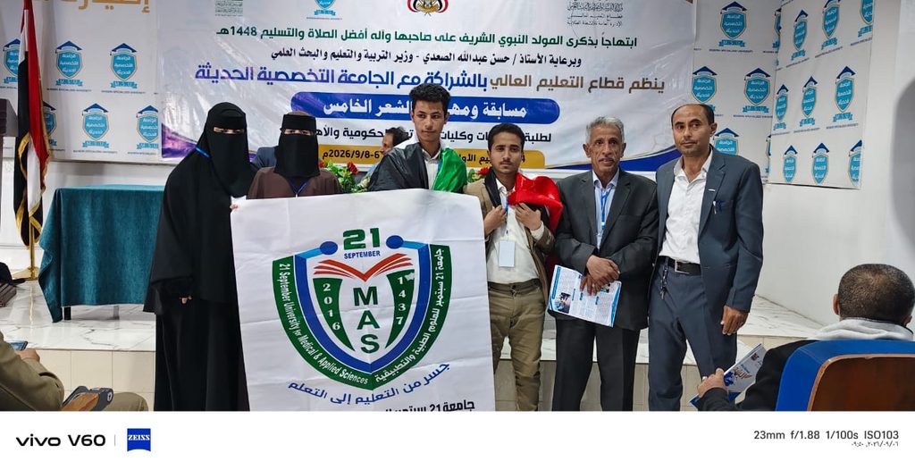 Group of people on a stage holding a banner with a university emblem (MAS) and a 21 Sept date, at a formal event backdrop with Arabic text.