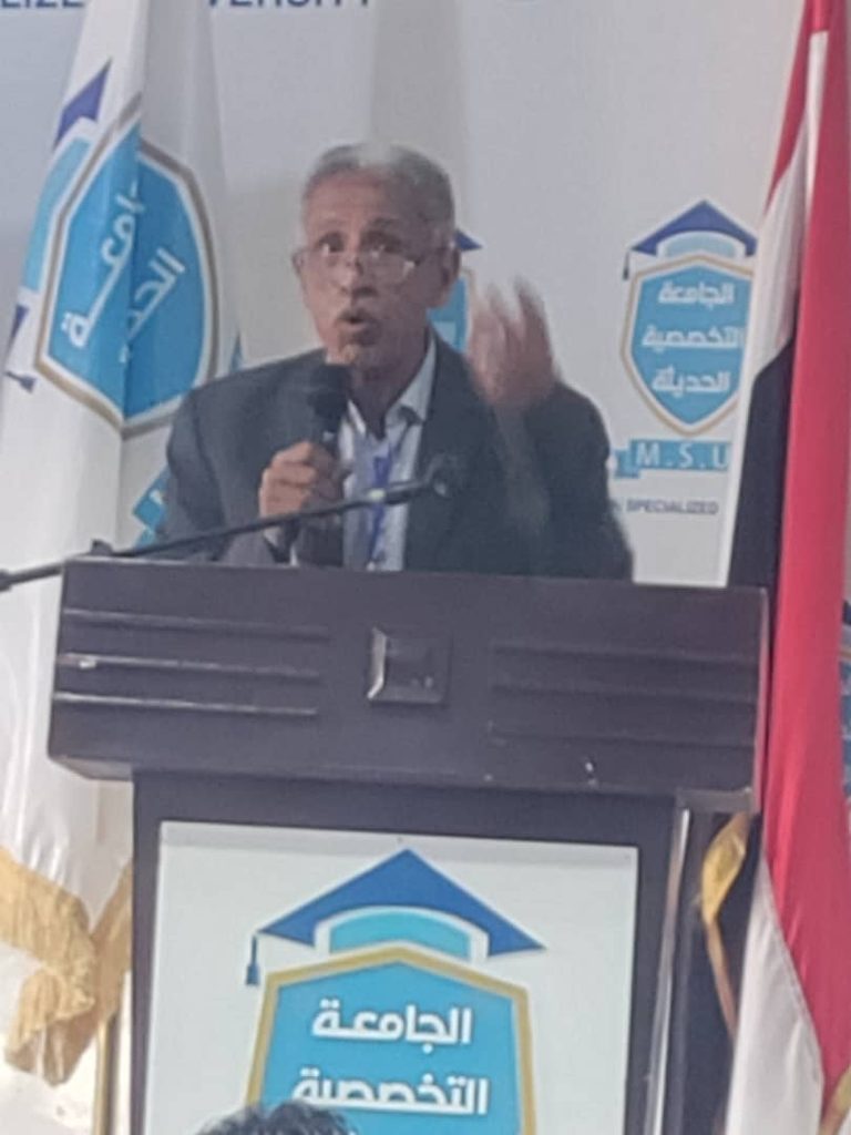 Man in a suit giving a speech at a podium, microphone in hand, gesturing with his other hand.