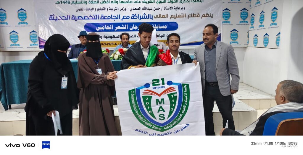 Group of students and faculty on a stage posing with a large MAS banner during a university event or ceremony.
