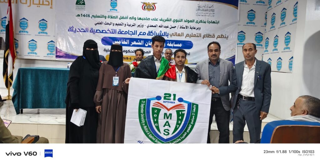Group of people on a stage holding a white banner with a green MAS emblem at a university ceremony.