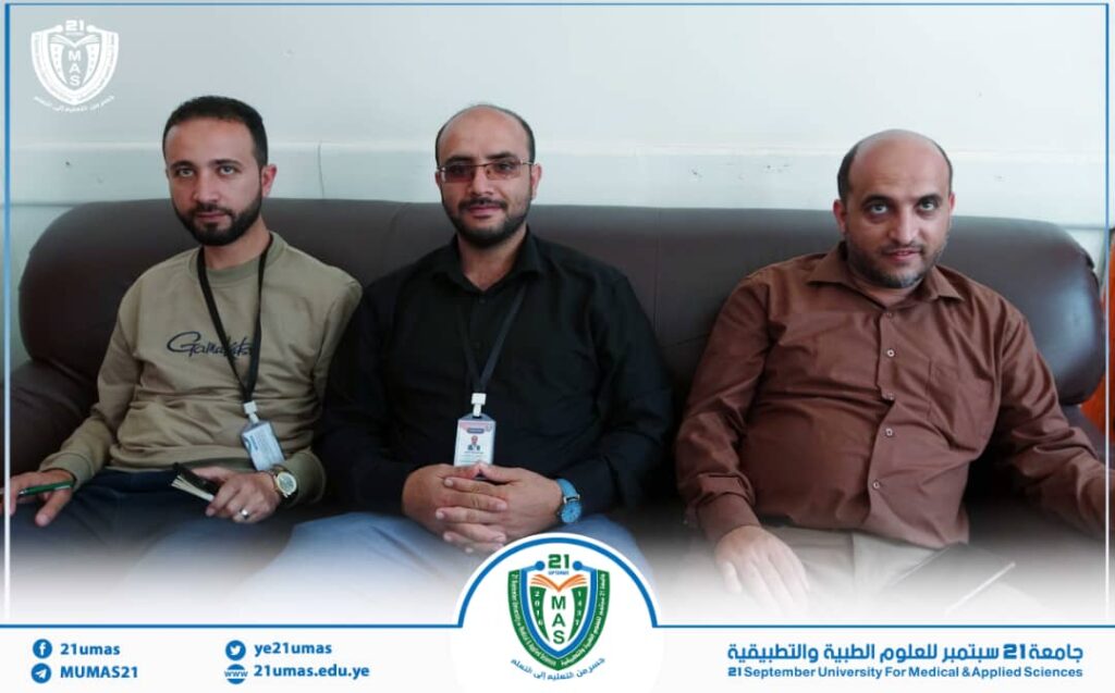 Three men with ID badges sit on a dark leather sofa in a university setting, posing for a group photo with a blue-and-white frame and official logo nearby.