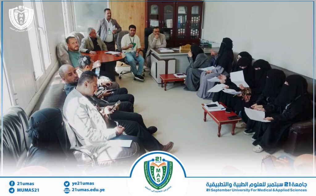 University staff and students hold a meeting in a bright room; men on the left, women in black abayas on the right, with a presenter at the back and a desk in the center.