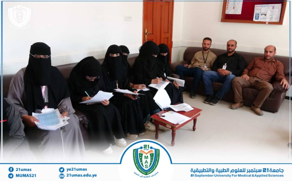 Group of women in black abayas and veils sit with notebooks, while three men sit on a sofa in a university office—everyone appears to be taking notes or listening.