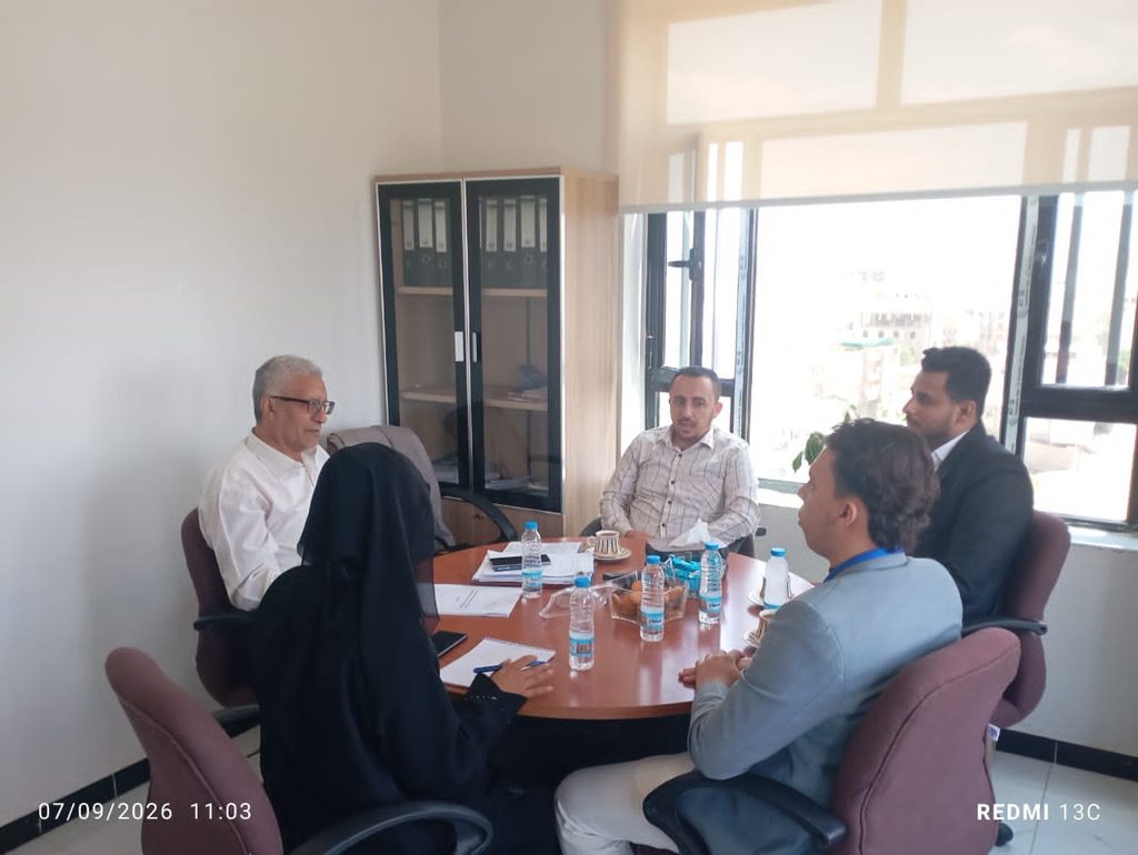 Five professionals seated around a round table in a bright office, discussing documents and with several water bottles on the table.