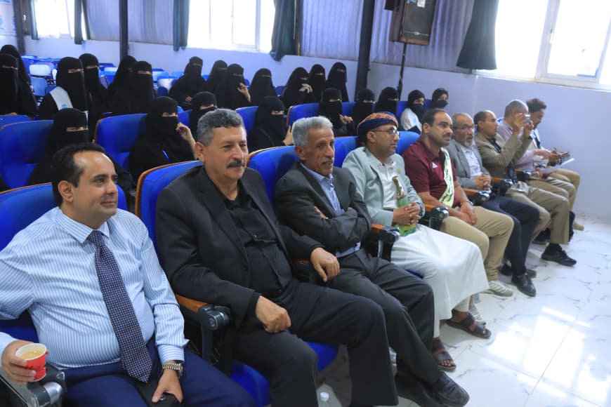 IMG-20260907-WA0066 - جامعة 21 سبتمبر Audience seated in a conference room: men in the front rows wearing suits and traditional dress, with women in black niqabs seated behind them.