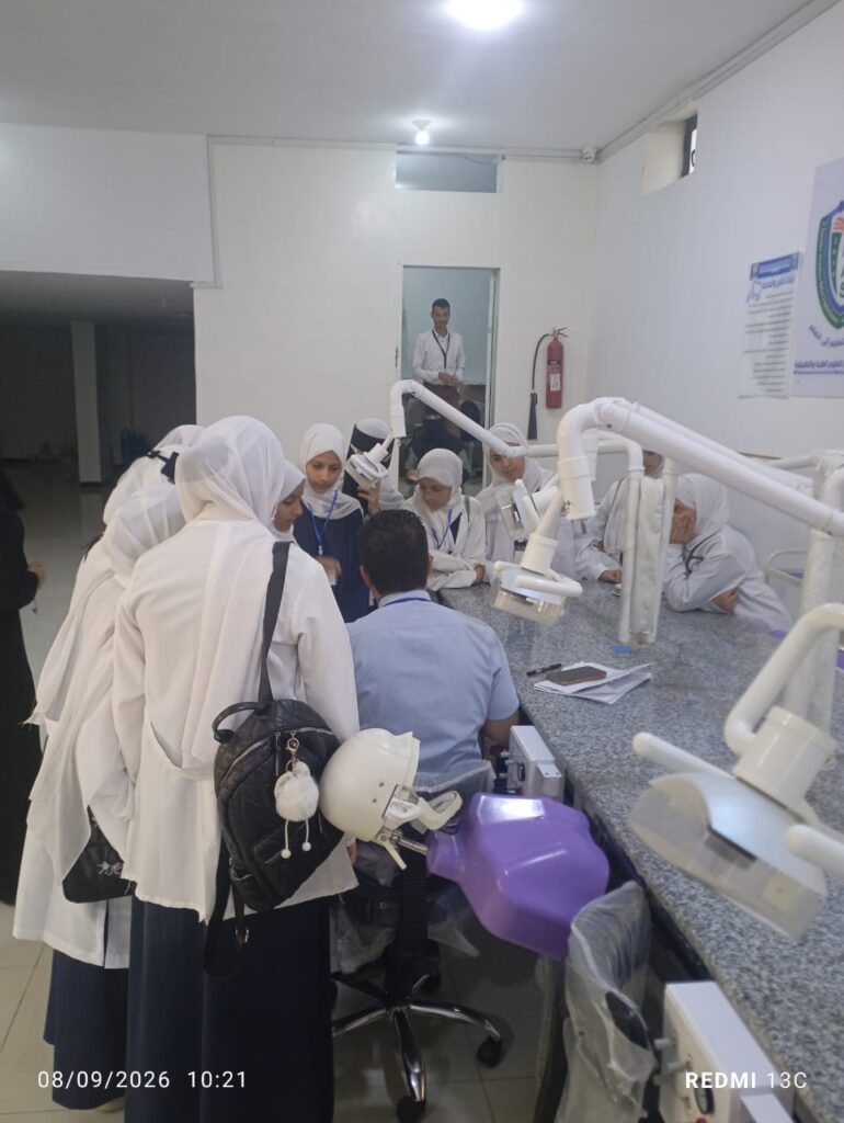 Group of female students in white hijabs gathered around a dental workbench with an instructor in a clinical training room.