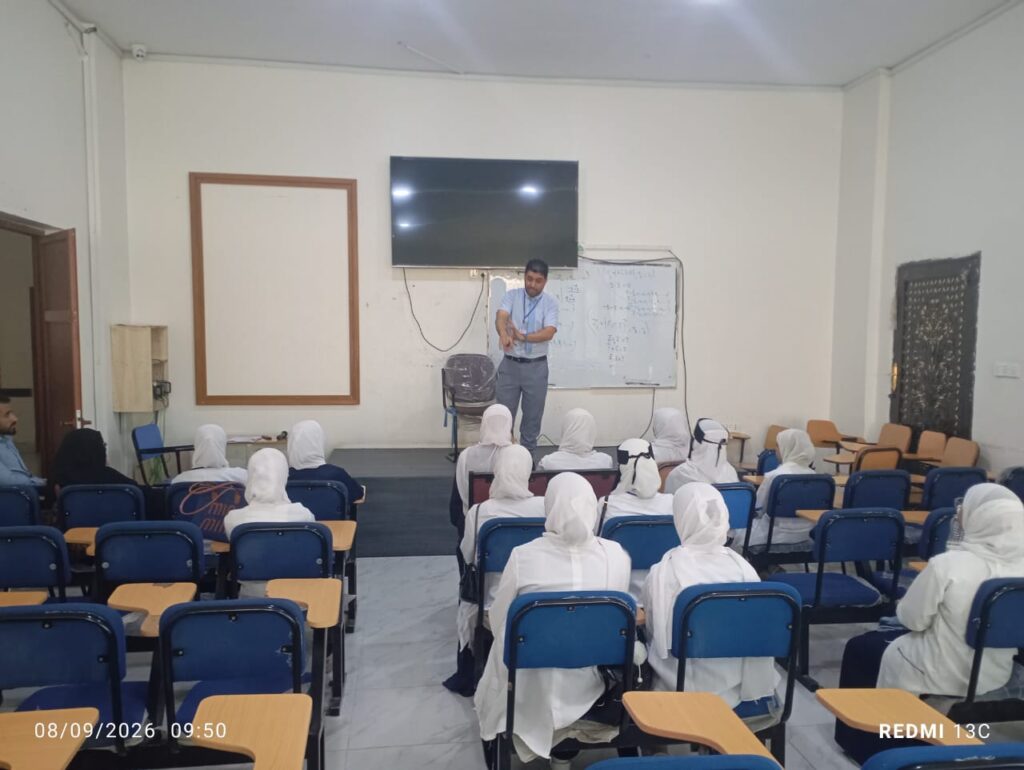 Instructor presents a lesson at the front of a classroom with students in white uniforms seated in blue desks; whiteboard with math equations behind him.