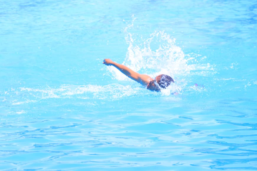 Swimmer in a blue pool performing a freestyle stroke, arm extended forward with splash behind them