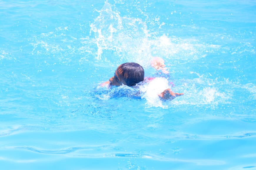 Person swimming in a bright blue pool, performing a stroke with splashes around them