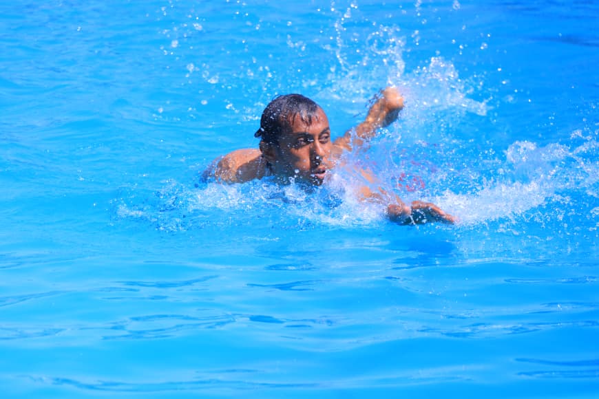 Man swimming in a bright blue pool, splashing water as he moves his arms.