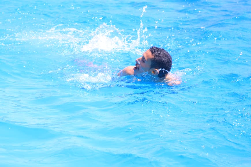 Man swimming in bright blue pool with head above water and splashes around him for a dynamic moment.