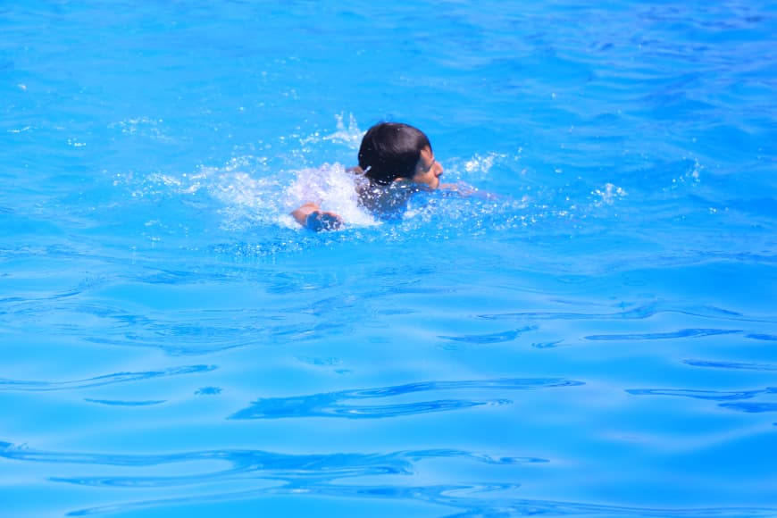 Person swimming in a bright blue pool, head above water and arm moving forward after a stroke.