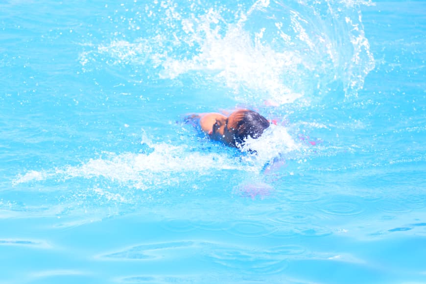 Swimmer in a bright blue pool creating a large splash as arms pull through the water