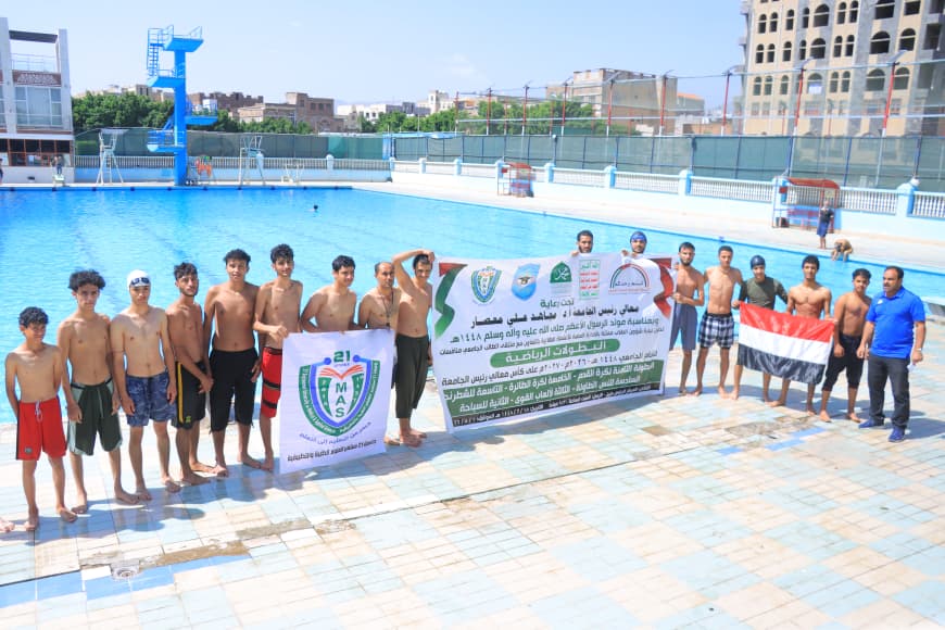Group of young swimmers in swimwear posing by a large outdoor pool, holding event banners and the Egyptian flag in the foreground.
