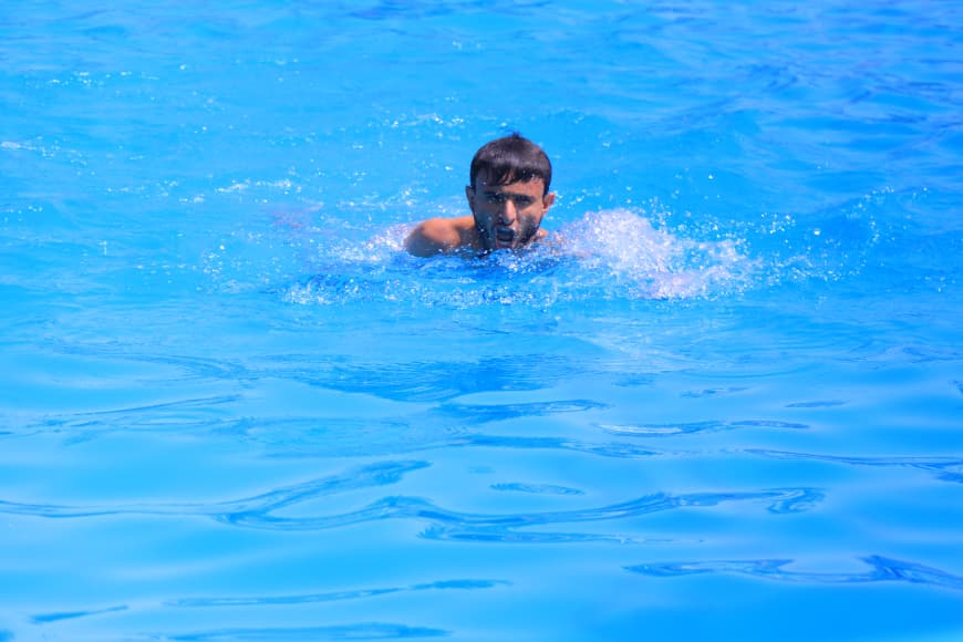 Man swimming in a bright blue pool, head above water with splashing around him