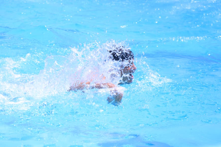 Person swimming front crawl in a bright blue pool with splashing water around the head and arm.