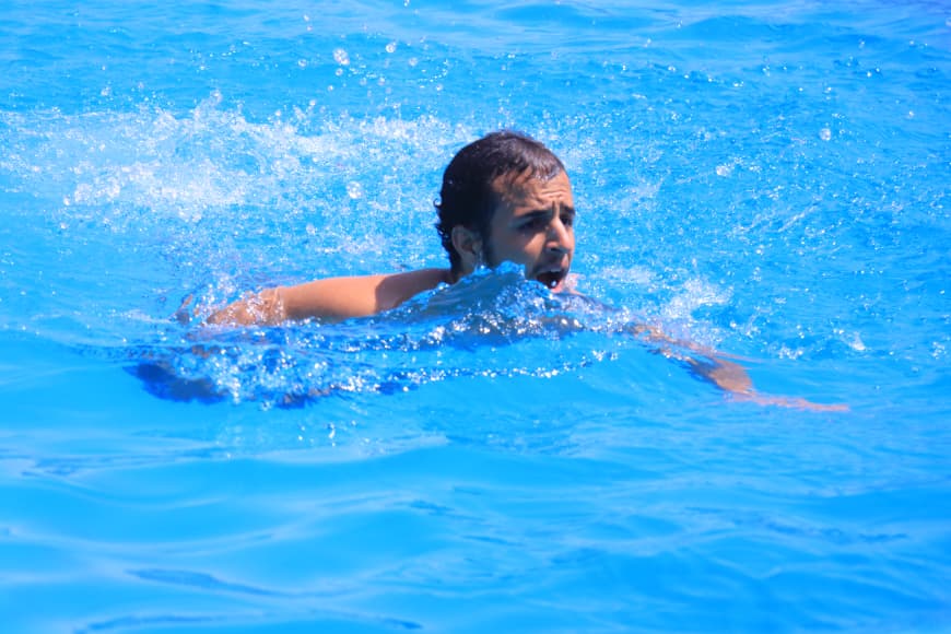 Man swimming in a bright blue pool, head above water as splashes surround him.