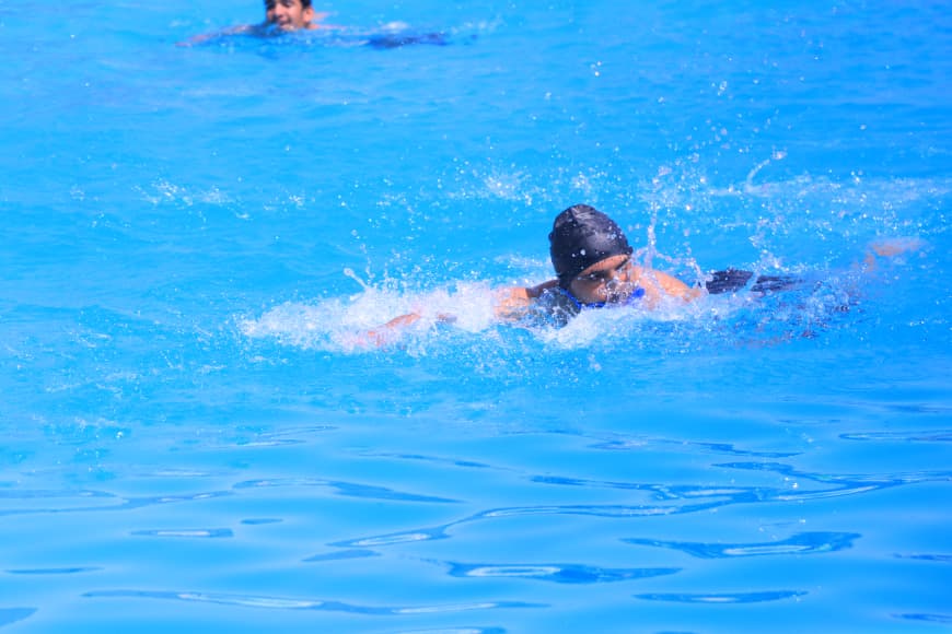 Swimmer in a black swim cap paddling through bright blue water with splashes around.