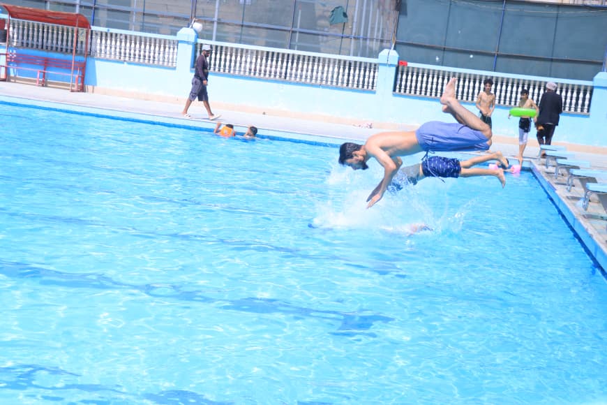Male swimmer dives headfirst into a bright blue pool from the edge, creating a splash in midair.