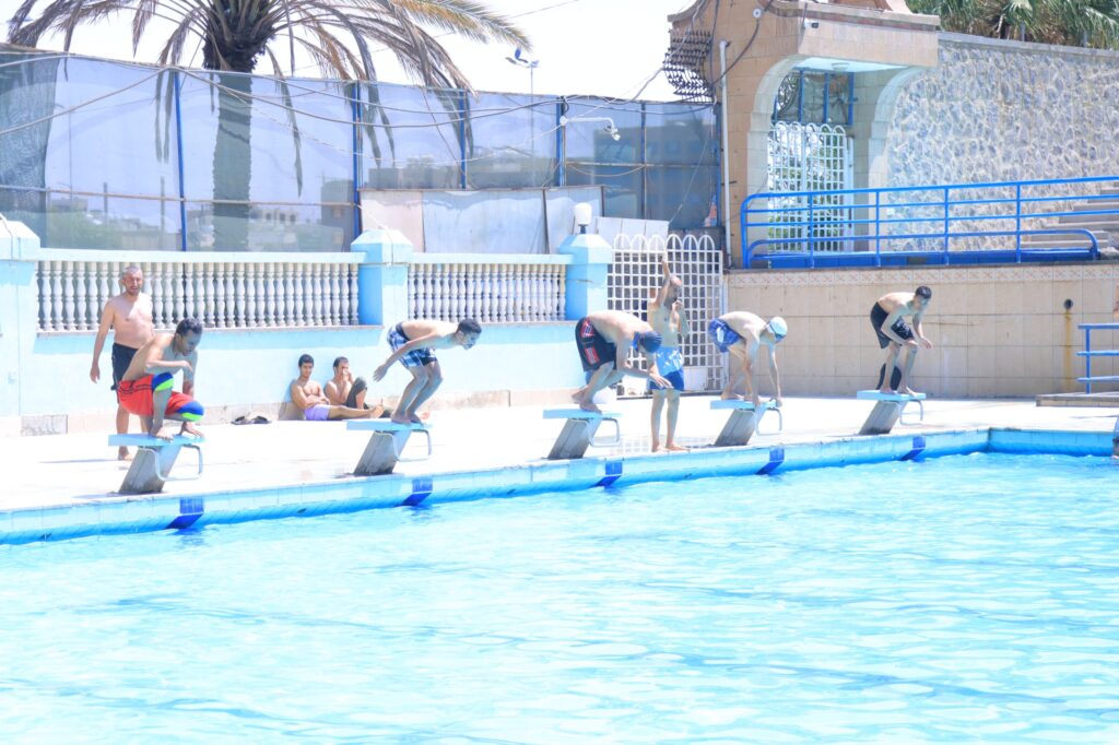 Group of boys on starting blocks about to dive into a bright blue pool on a sunny day.