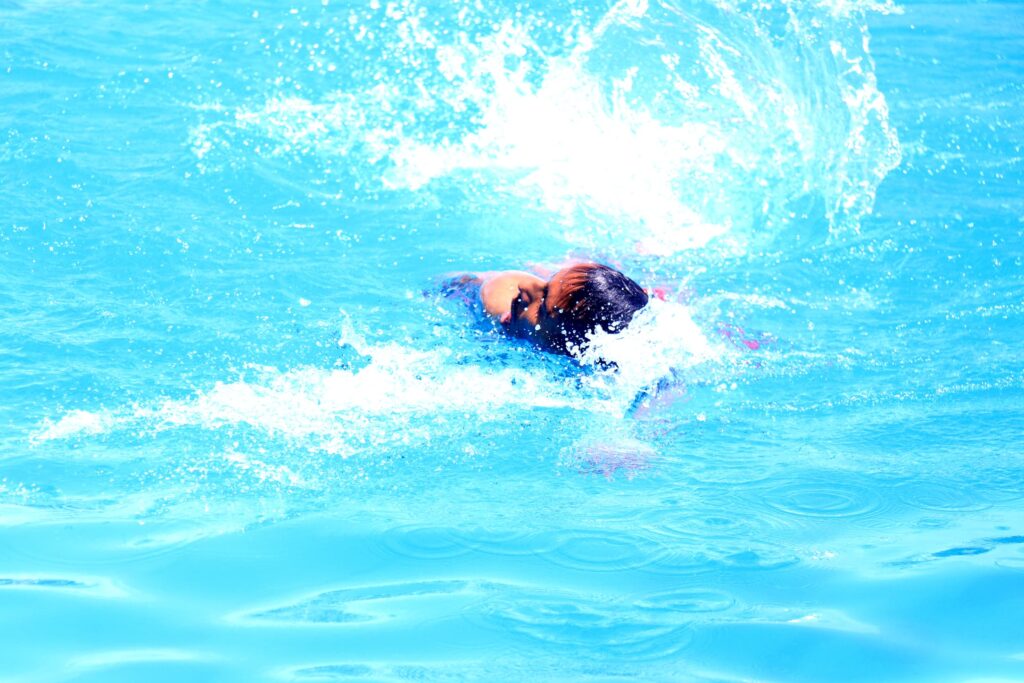Swimmer in a bright blue pool creating a splash with water around their head.