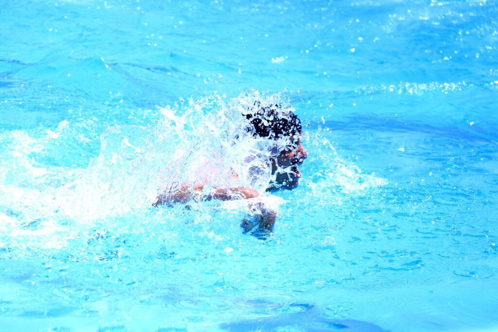 Person splashing in a bright blue swimming pool with water droplets around the head area