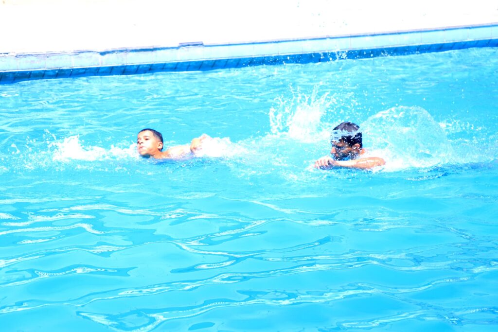 Two people swimming and splashing in a bright blue pool near the edge.