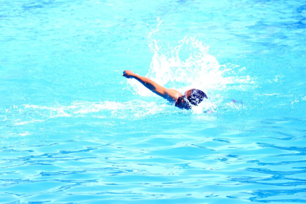 Swimmer in a bright blue pool extending an arm forward with spray around them