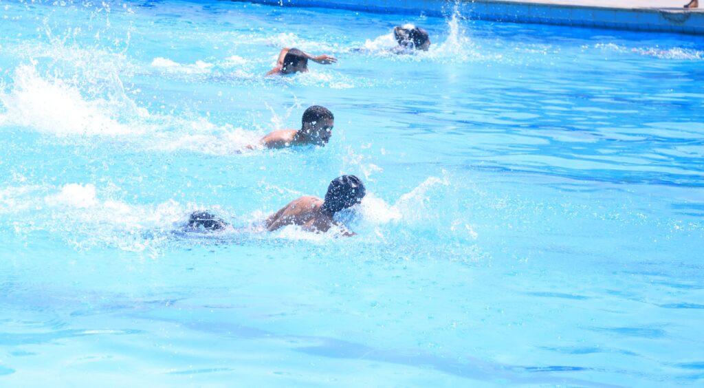 Several people swim in a bright blue pool, splashing water as they move.