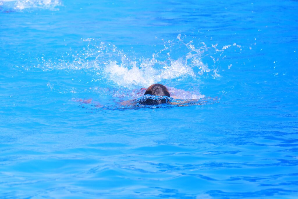 Swimmer's head surfacing in a bright blue pool with water splashes around it