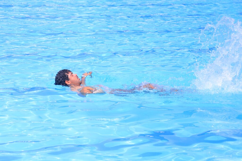 Man swimming in a bright blue pool with water splashing on the right side.